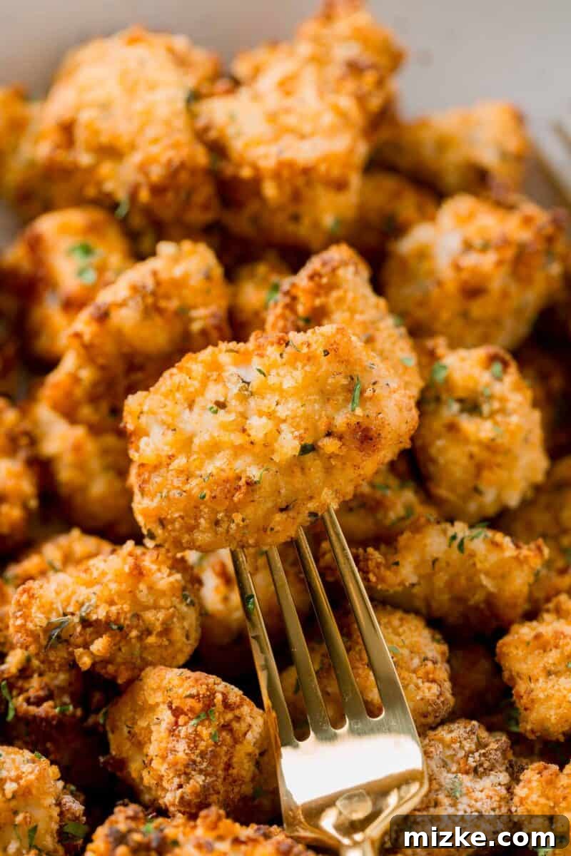 A single air-fried chicken nugget delicately held on a gold fork, resting on a pile of other perfectly cooked nuggets