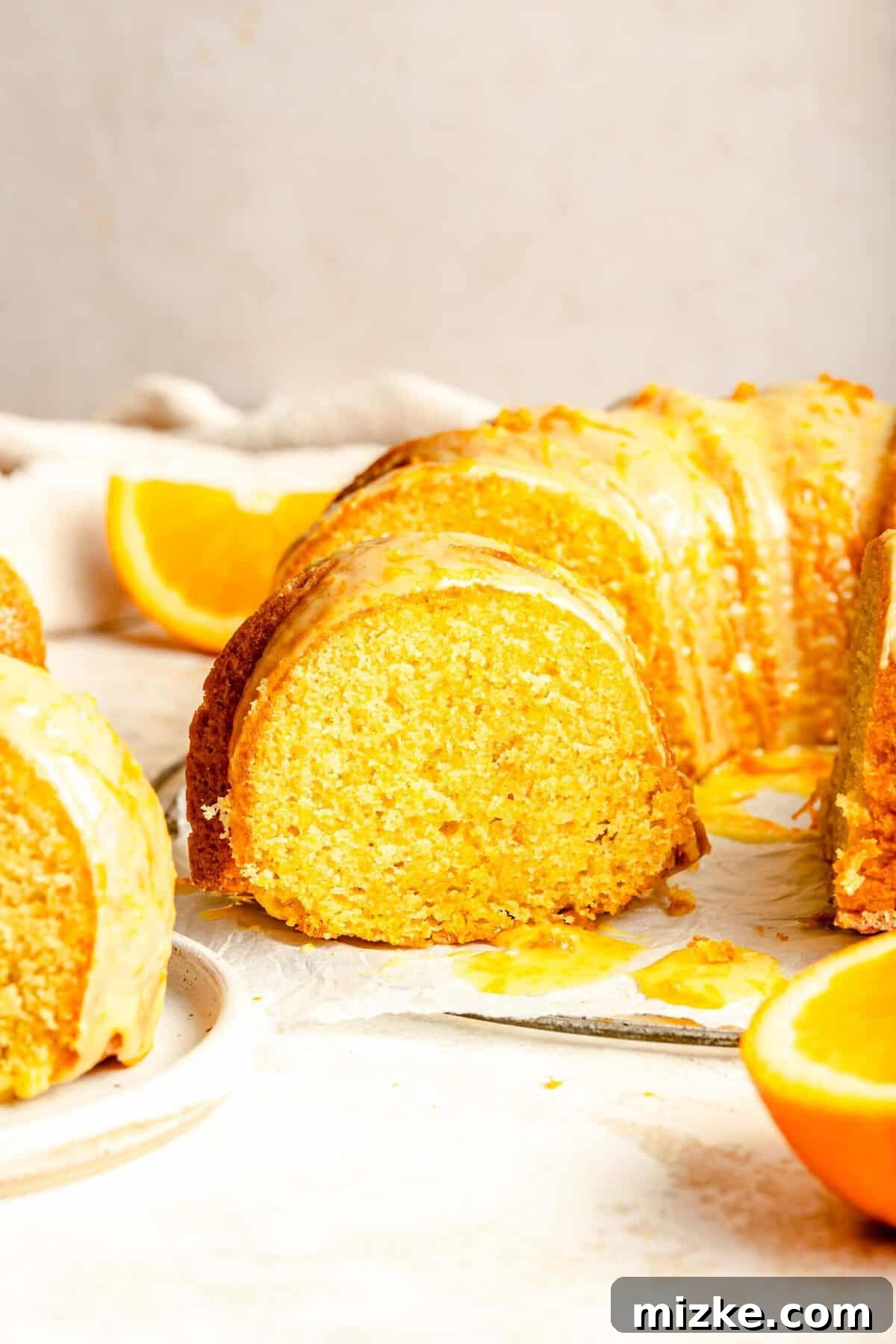Enjoy a perfect slice of this tender, buttery orange pound cake, generously coated with a sweet orange glaze, truly loaded with fresh citrus flavor. A beautifully cut slice of the moist orange pound cake, revealing its tender crumb and glistening glaze, elegantly served on a white plate with fresh zest.
