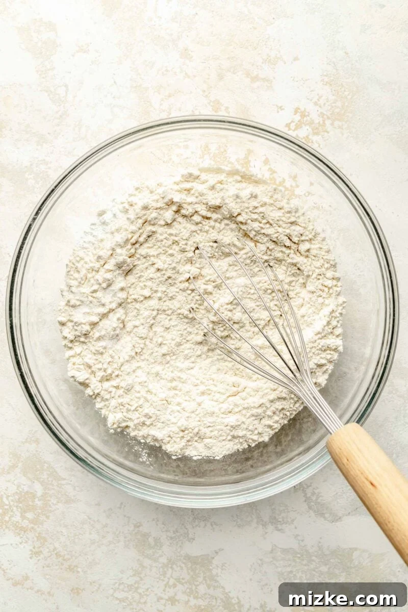 Thoroughly whisk together the flour, salt, baking soda, and baking powder for the essential dry ingredients. A bowl filled with the whisked dry ingredients: all-purpose flour, salt, baking soda, and baking powder, prepared for the orange pound cake recipe.