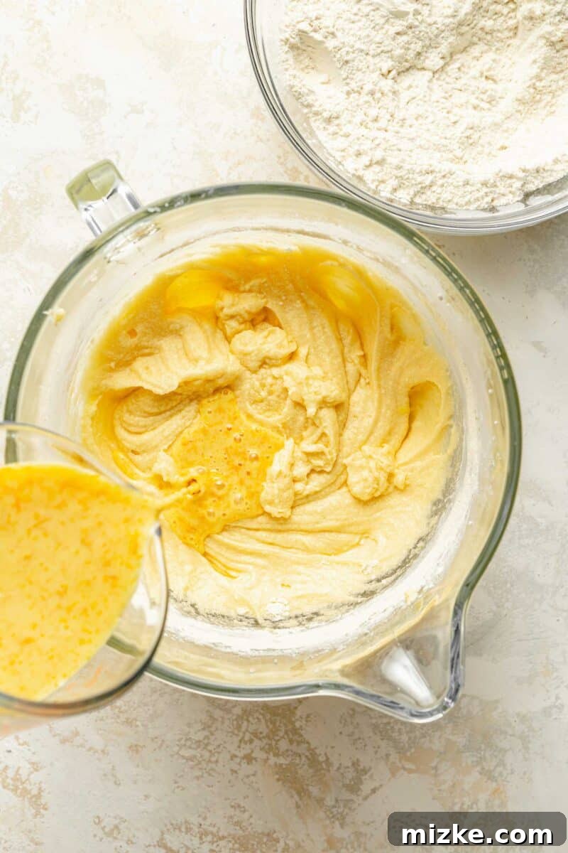 Carefully alternate adding the wet and dry ingredients to the rich orange pound cake batter, mixing gently for optimal texture. A detailed shot showing the process of alternately adding the fragrant wet mixture and the sifted dry ingredients into the orange pound cake batter in a stand mixer.