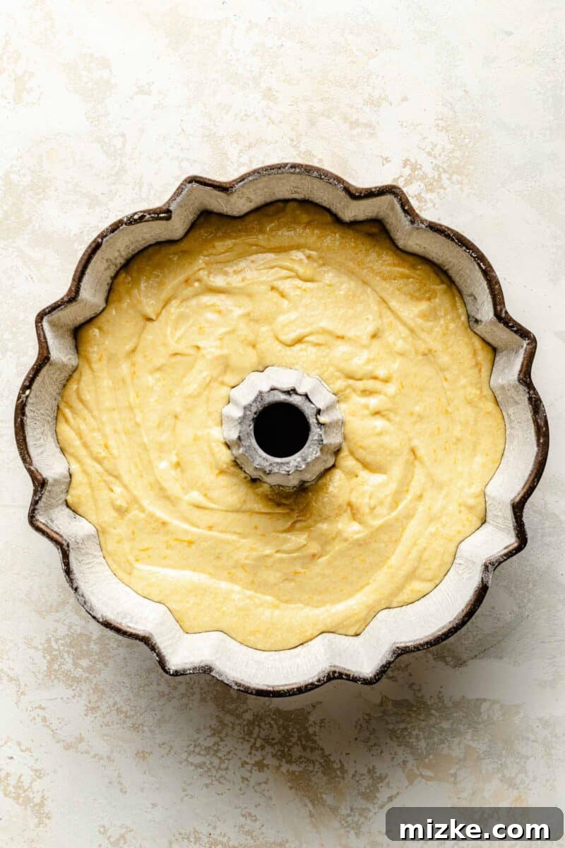 The vibrant orange pound cake batter now perfectly settled in a bundt pan, awaiting its delicious transformation in the oven. Smooth, vibrant orange pound cake batter perfectly poured into a meticulously greased and floured bundt pan, ready for its journey into the oven.