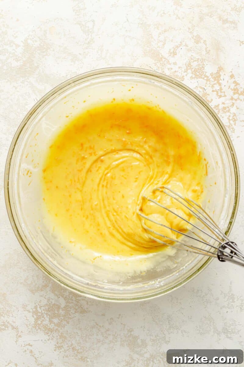 Whip up the vibrant orange glaze by whisking together fresh orange zest, powdered sugar, and tangy orange juice. A bowl of freshly whisked orange glaze, smooth, glossy, and perfectly ready to be poured over the cooled orange pound cake.