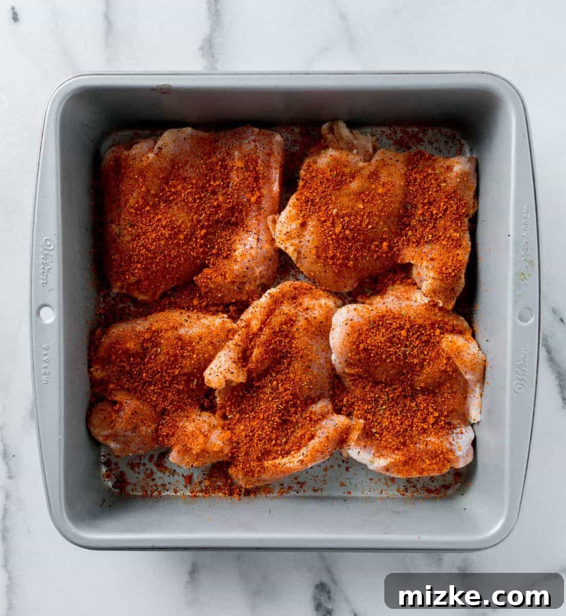 chicken thighs with dry rub sprinkled on top in a metal baking pan