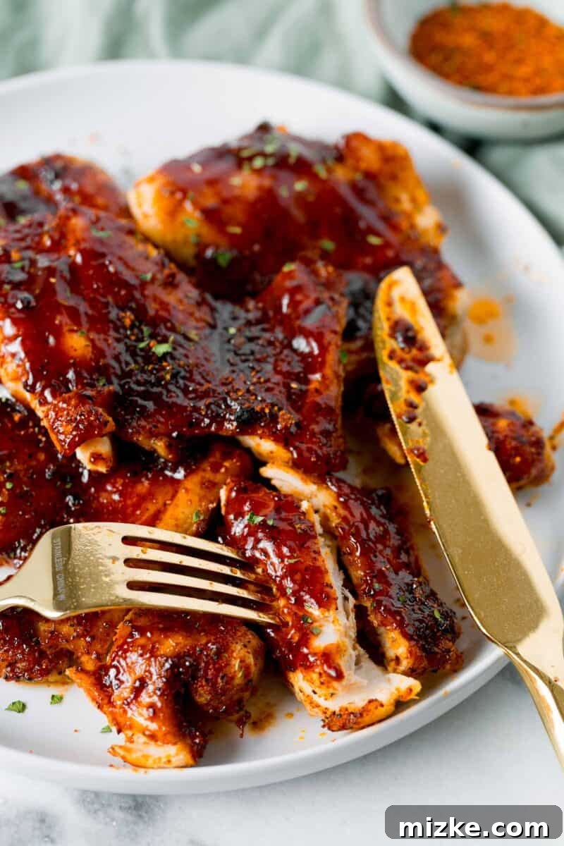 sliced bbq chicken thighs on a white plate with a gold knife and fork
