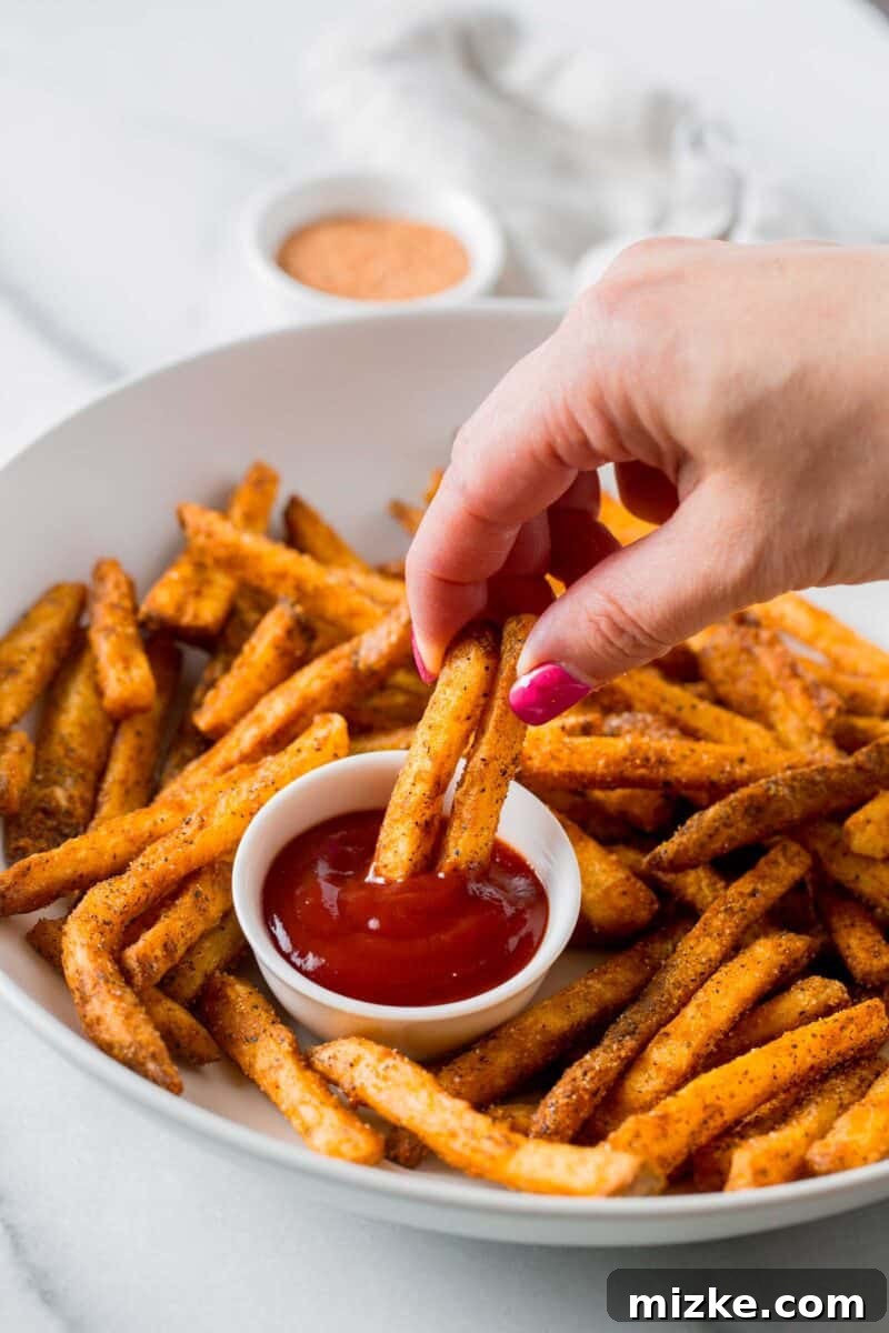 Louisiana Kick Fries 5 a hand is holding two fries and dipping into ketchup on a plate of cajun fries
