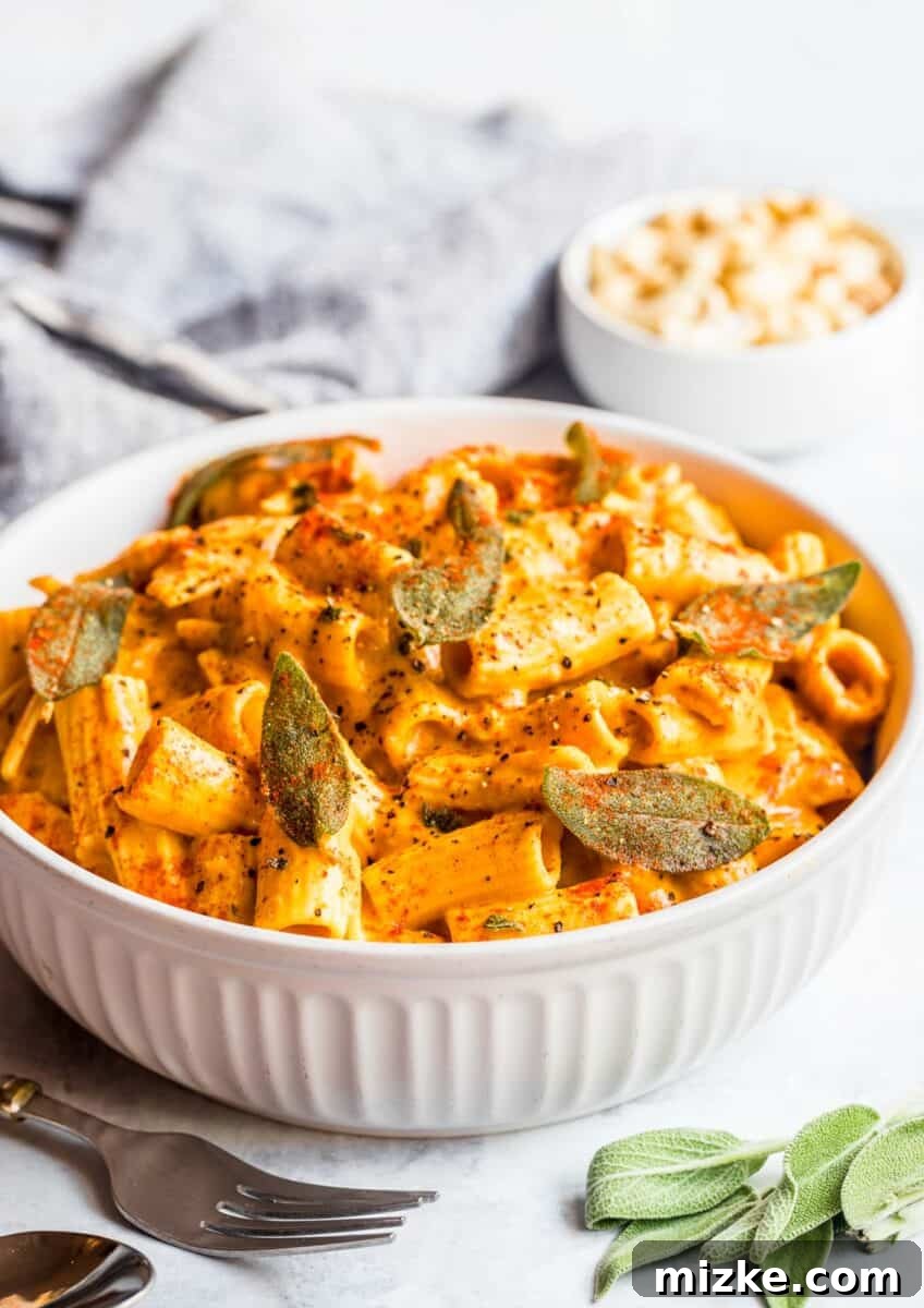 Velvet Vegan Pumpkin Pasta 4 Rigatoni pasta in a creamy vegan pumpkin sauce, served in a large white bowl, beautifully topped with crispy sage, a sprinkle of fresh paprika, and ground black pepper. This inviting presentation highlights the dish's comforting appeal.