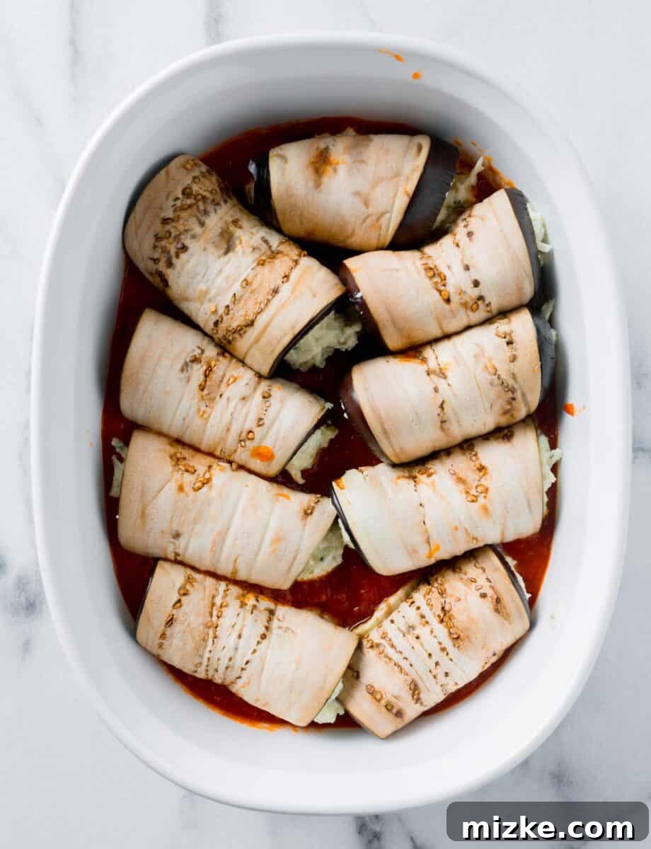 Golden Eggplant Spirals 6 Neatly rolled eggplant slices are arranged snugly in rows within a white casserole dish, awaiting their final toppings.