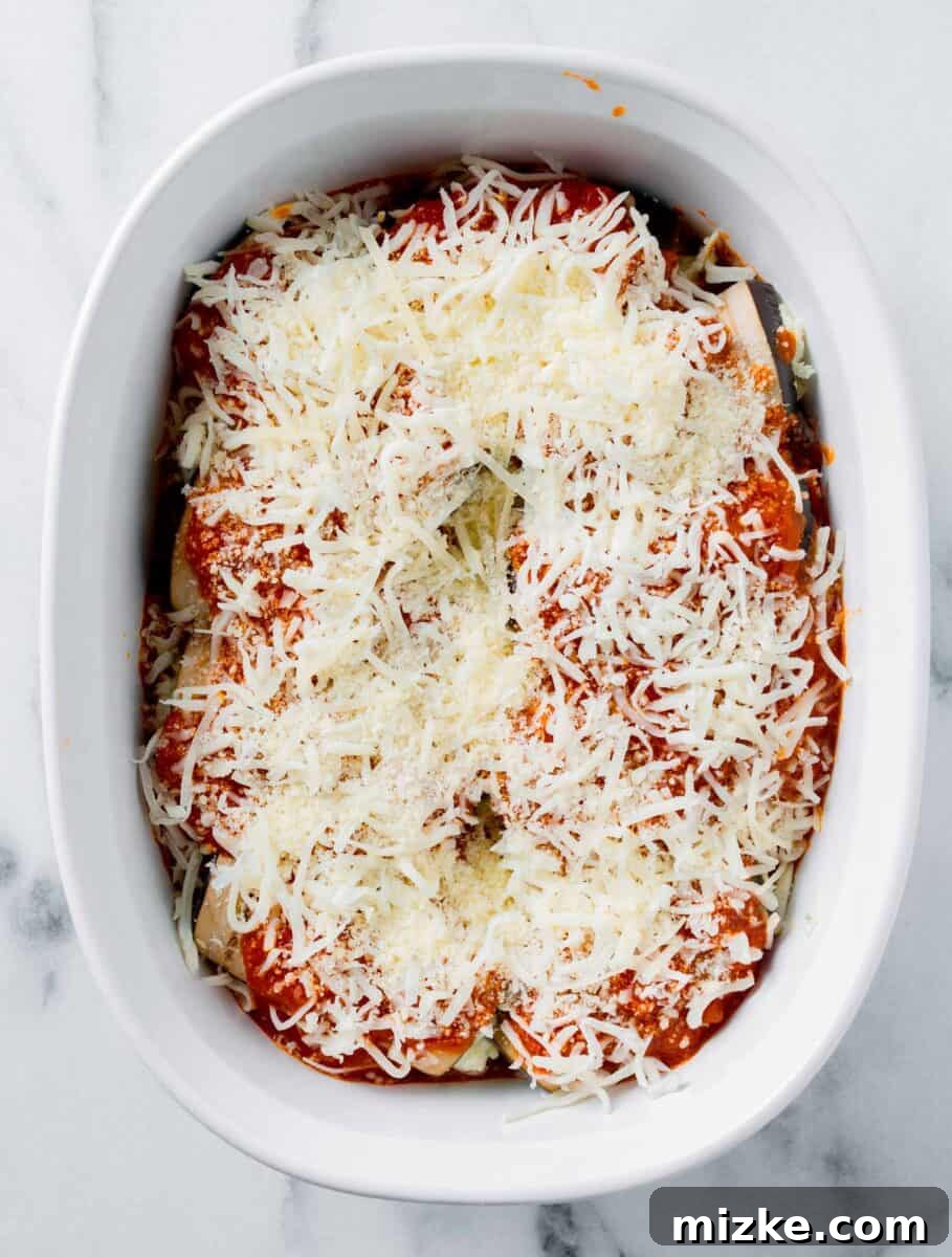 Golden Eggplant Spirals 7 A generous layer of shredded cheese is sprinkled across unbaked eggplant rollatini, promising a golden, bubbly top.