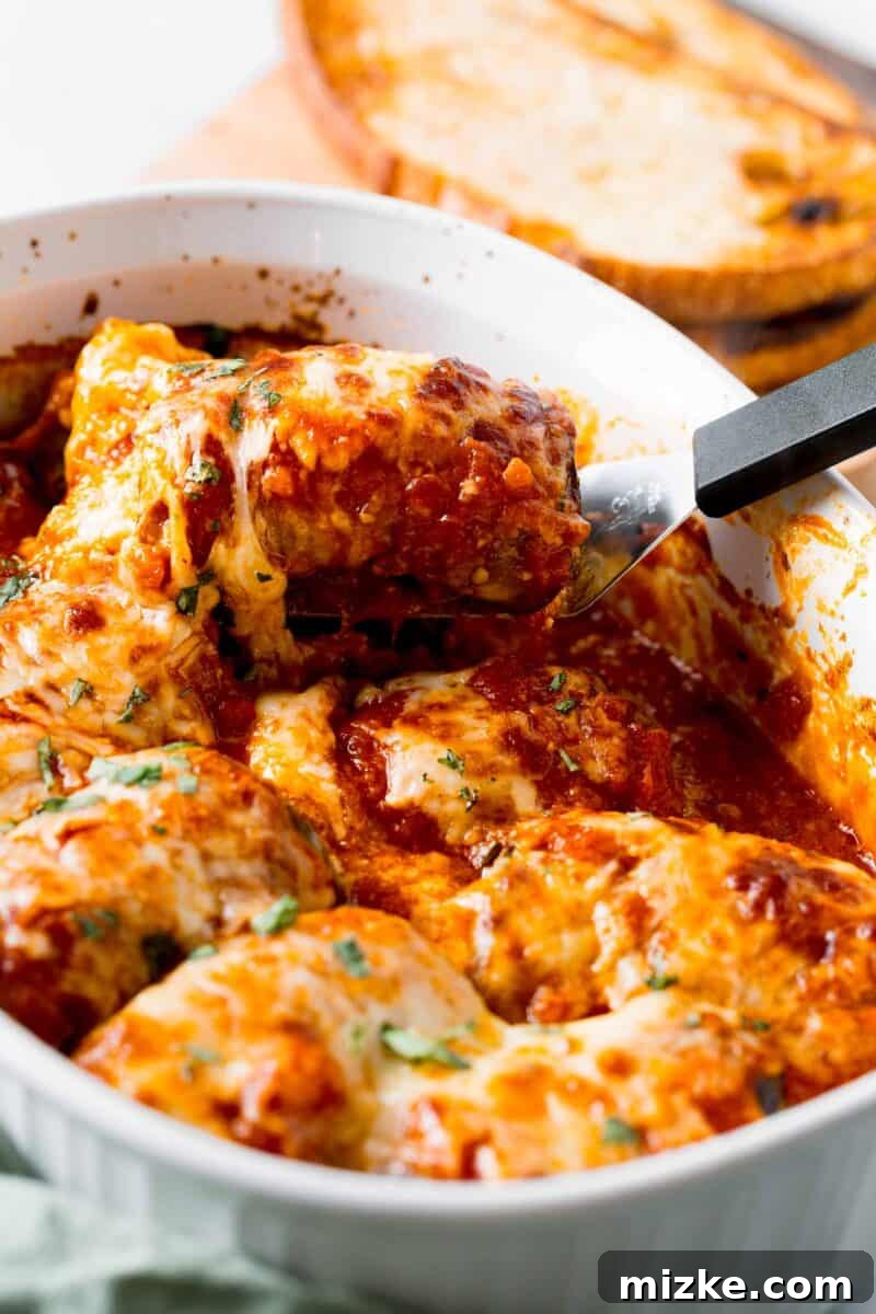 Golden Eggplant Spirals 9 A generous serving of baked eggplant rollatini is being carefully lifted from a baking dish, showcasing its layered goodness.