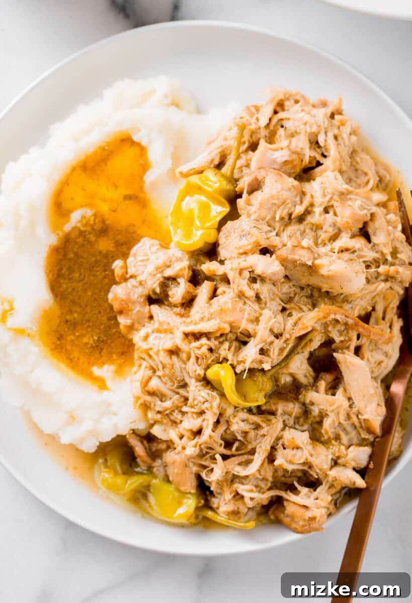 Zesty Mississippi Chicken 2 Mississippi chicken on a white rimmed plate with a side of creamy mashed potatoes and gravy, accompanied by a copper metal fork