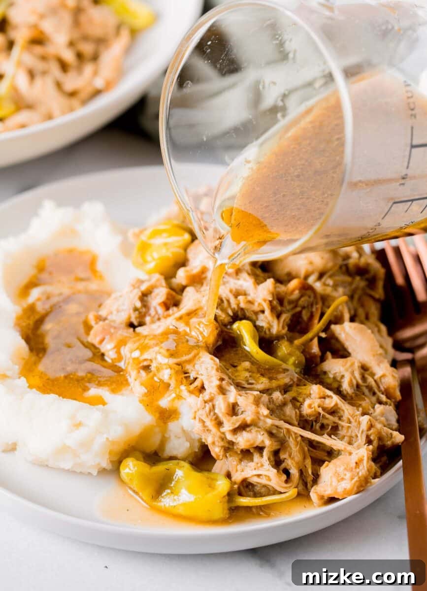 Zesty Mississippi Chicken 3 Pouring rich gravy over a serving of Mississippi chicken on a white plate, complemented by creamy mashed potatoes