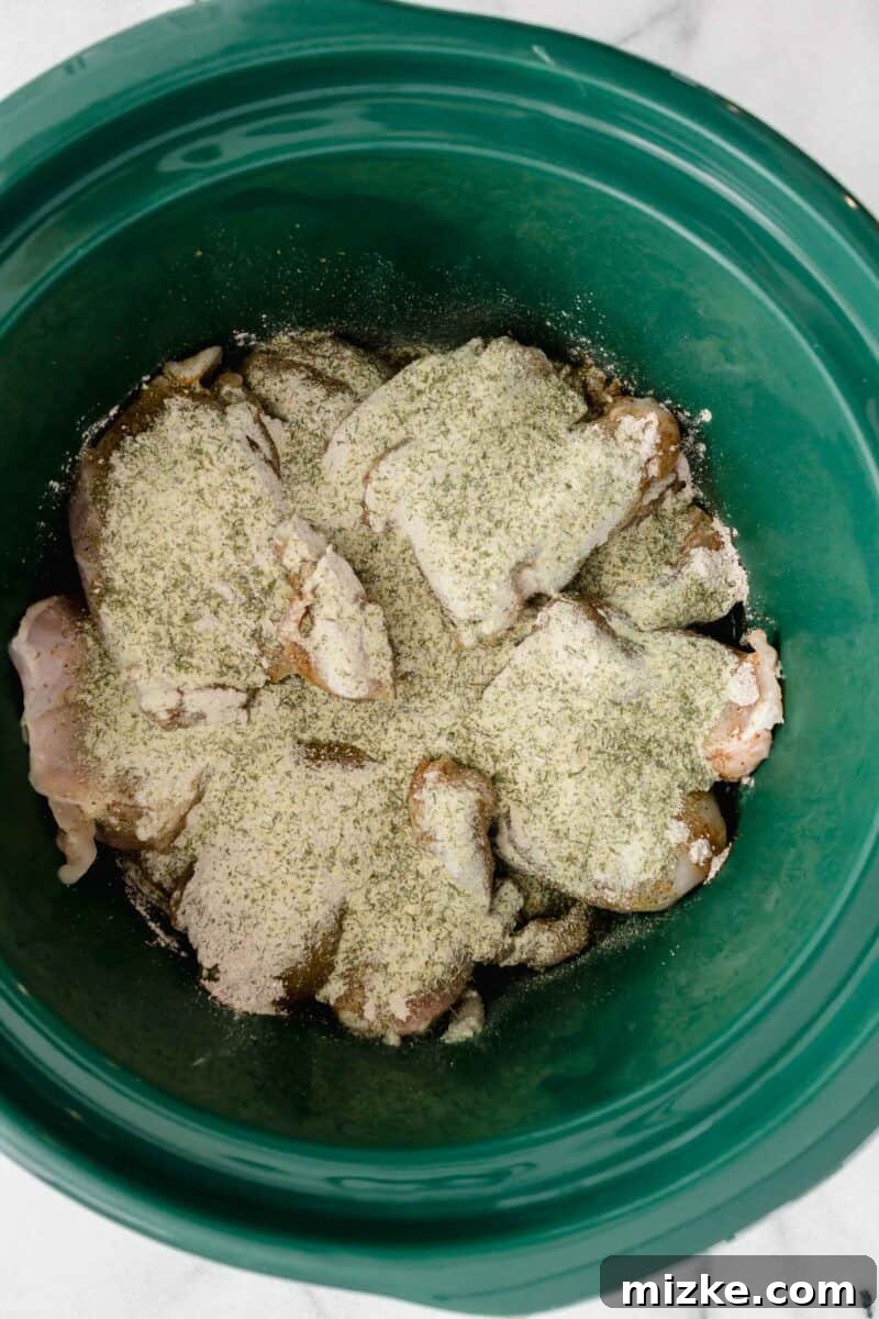 Zesty Mississippi Chicken 5 Chicken in a green ceramic slow cooker insert with au jus gravy mix and ranch seasoning sprinkled on top