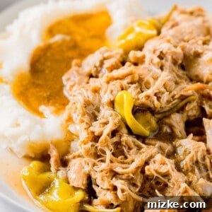 Mississippi chicken with pepperoncinis on a plate with mashed potatoes and gravy next to the chicken