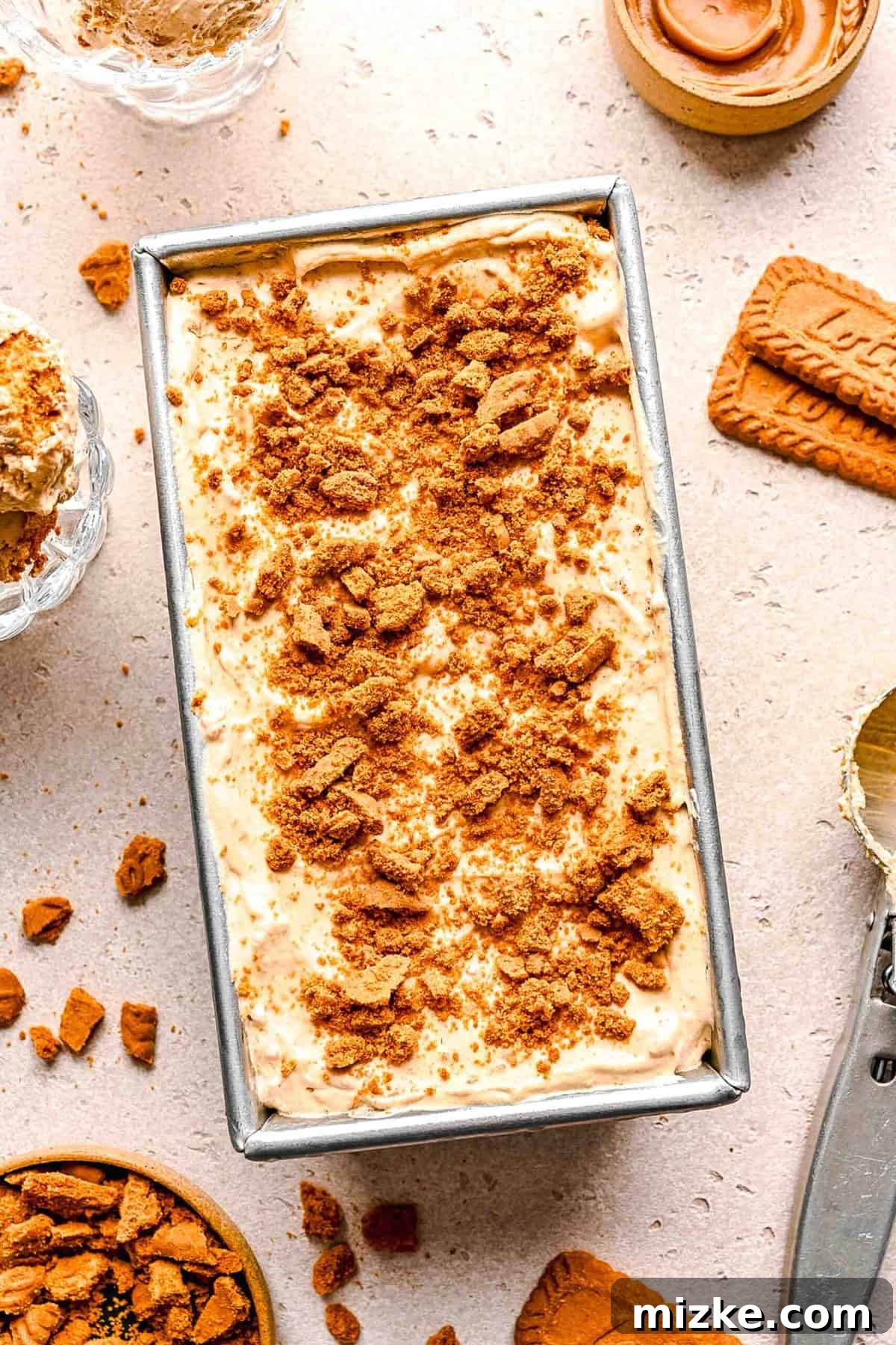 Biscoff ice cream in a loaf pan with cookies. An overhead shot of the Biscoff ice cream presented in a loaf pan, artfully surrounded by whole Biscoff cookies and a smattering of crumbs.