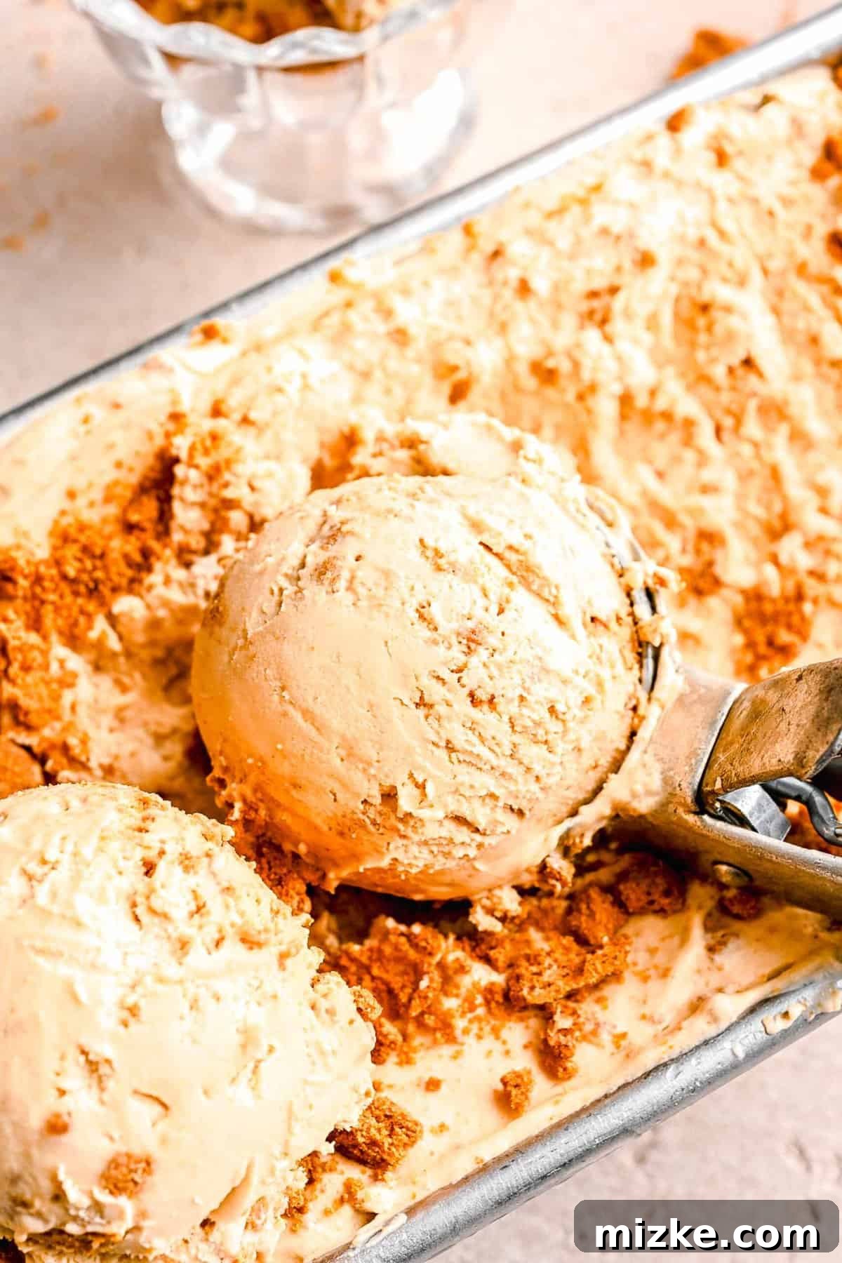 Scooping homemade Biscoff ice cream. An ice cream scoop digging into the perfectly set Biscoff ice cream in a loaf pan, revealing its creamy texture.