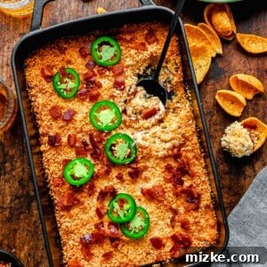 Overhead of jalapeno popper dip with a scoop taken out of it. A bowl of chips sits close by.