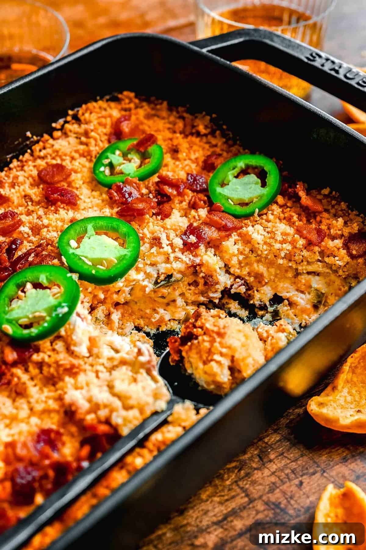A baking dish filled with Jalapeño Popper Dip, showcasing its rich, melted cheese and crispy topping, with a few portions scooped out.