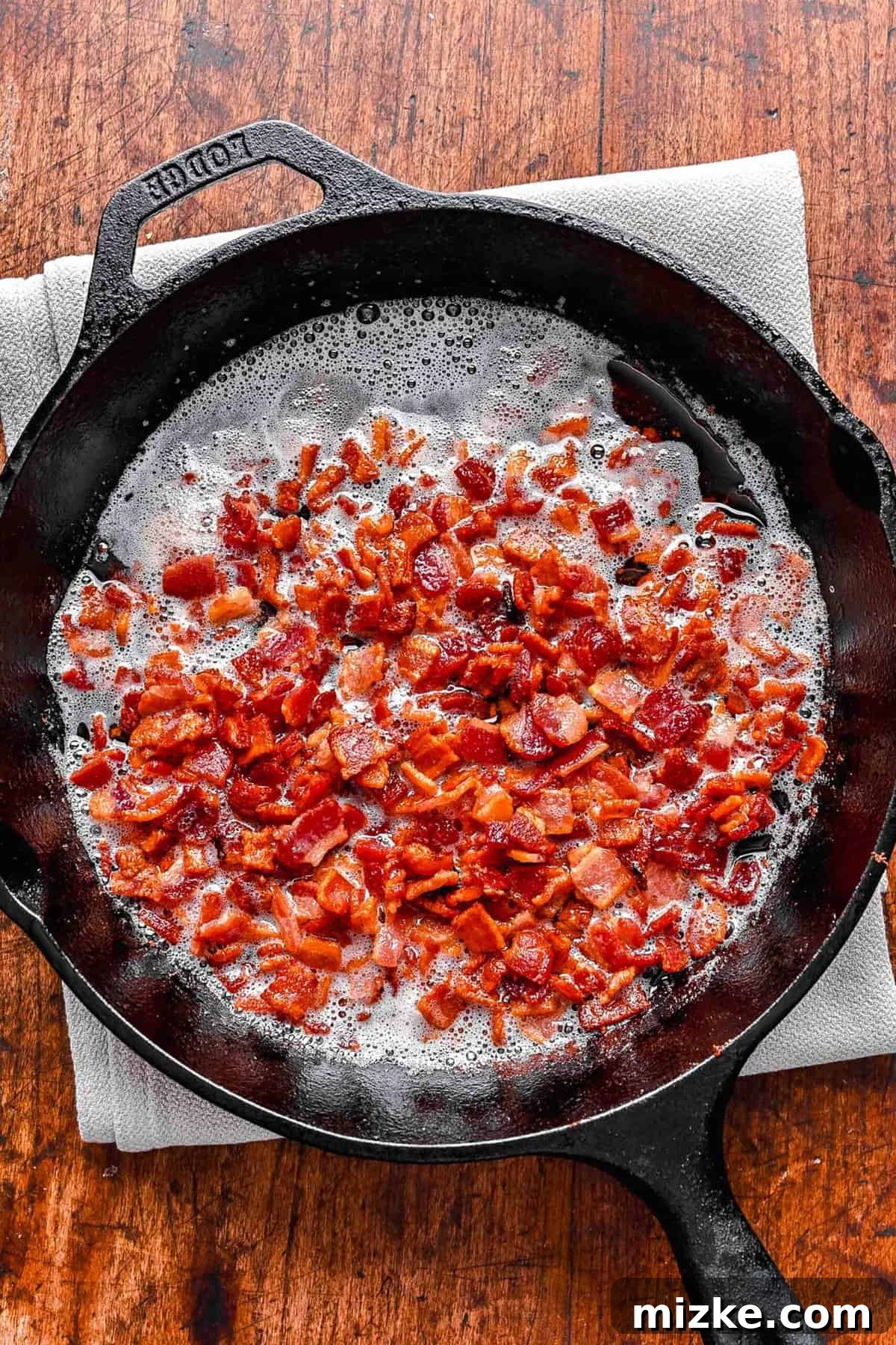 Crispy diced bacon cooking in a hot skillet on the stovetop.