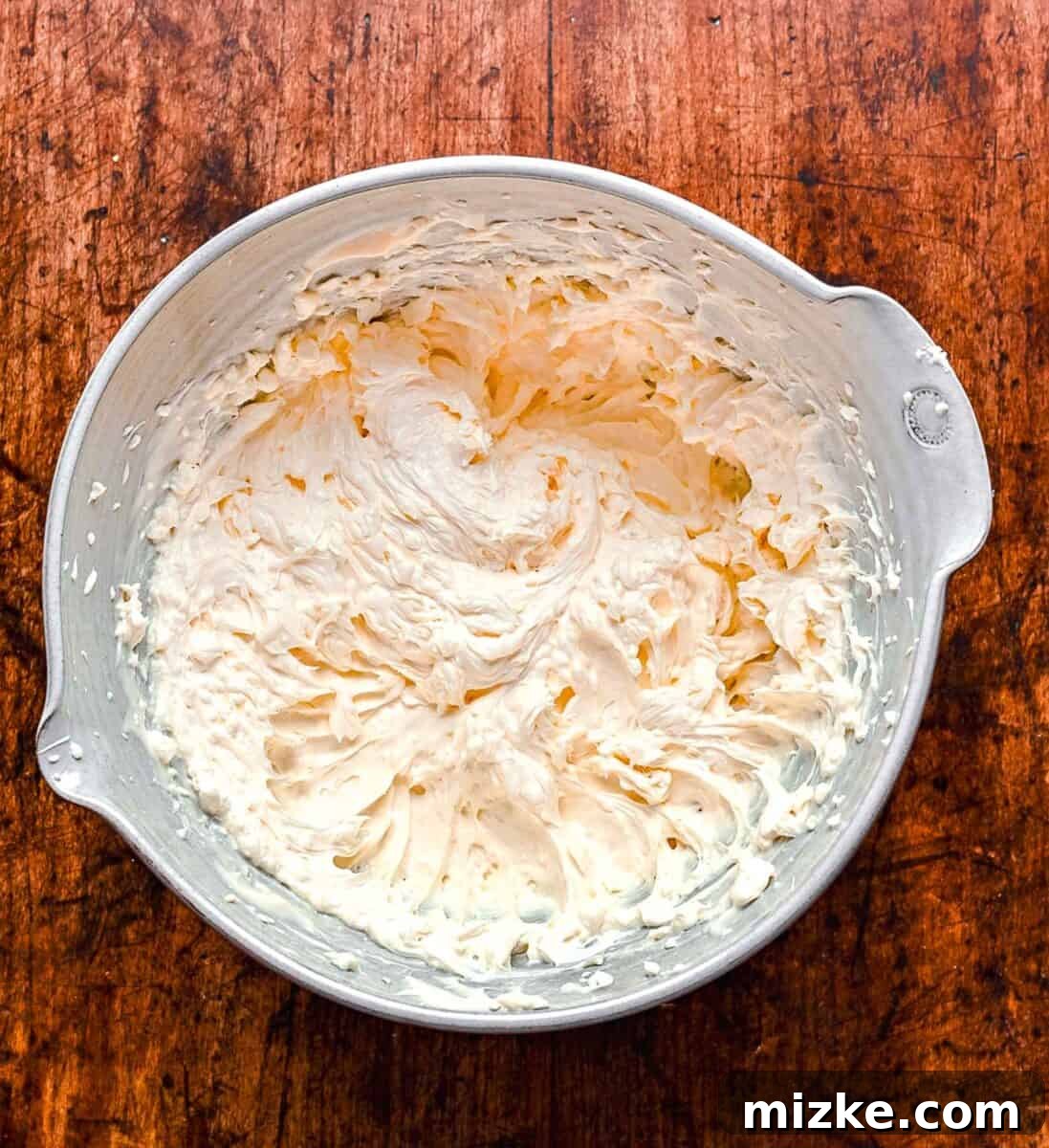 Cream cheese and mayonnaise being blended together in a mixing bowl until smooth.