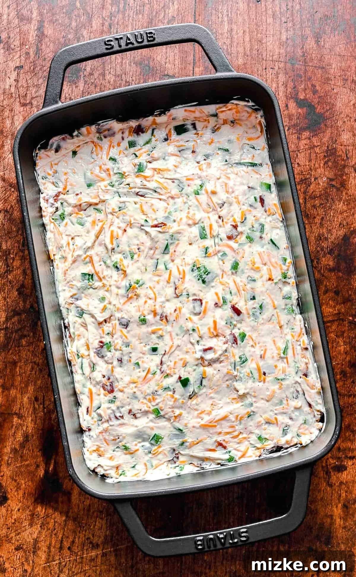 Jalapeño Popper Dip mixture in a baking dish, topped with the panko-parmesan mixture, ready to be baked.