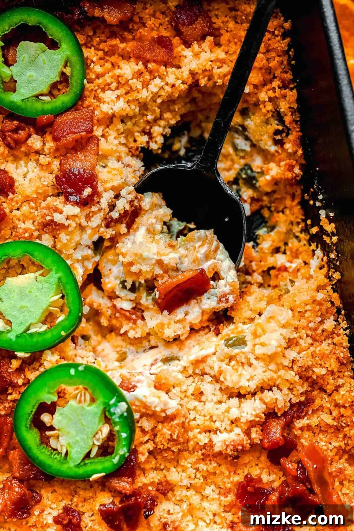 A scoop being taken out of the hot, bubbly Jalapeño Popper Dip in a baking dish.