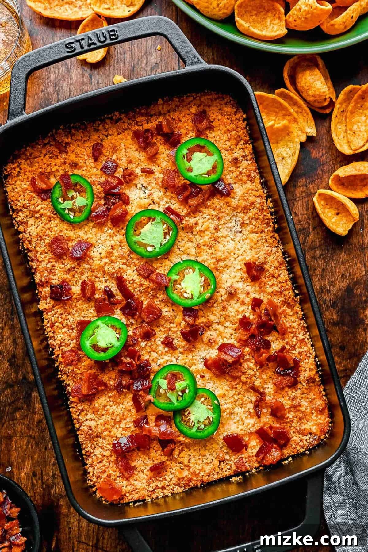 Overhead shot of the entire Jalapeño Popper Dip in its baking dish, next to a bowl of chips, ready to be served.