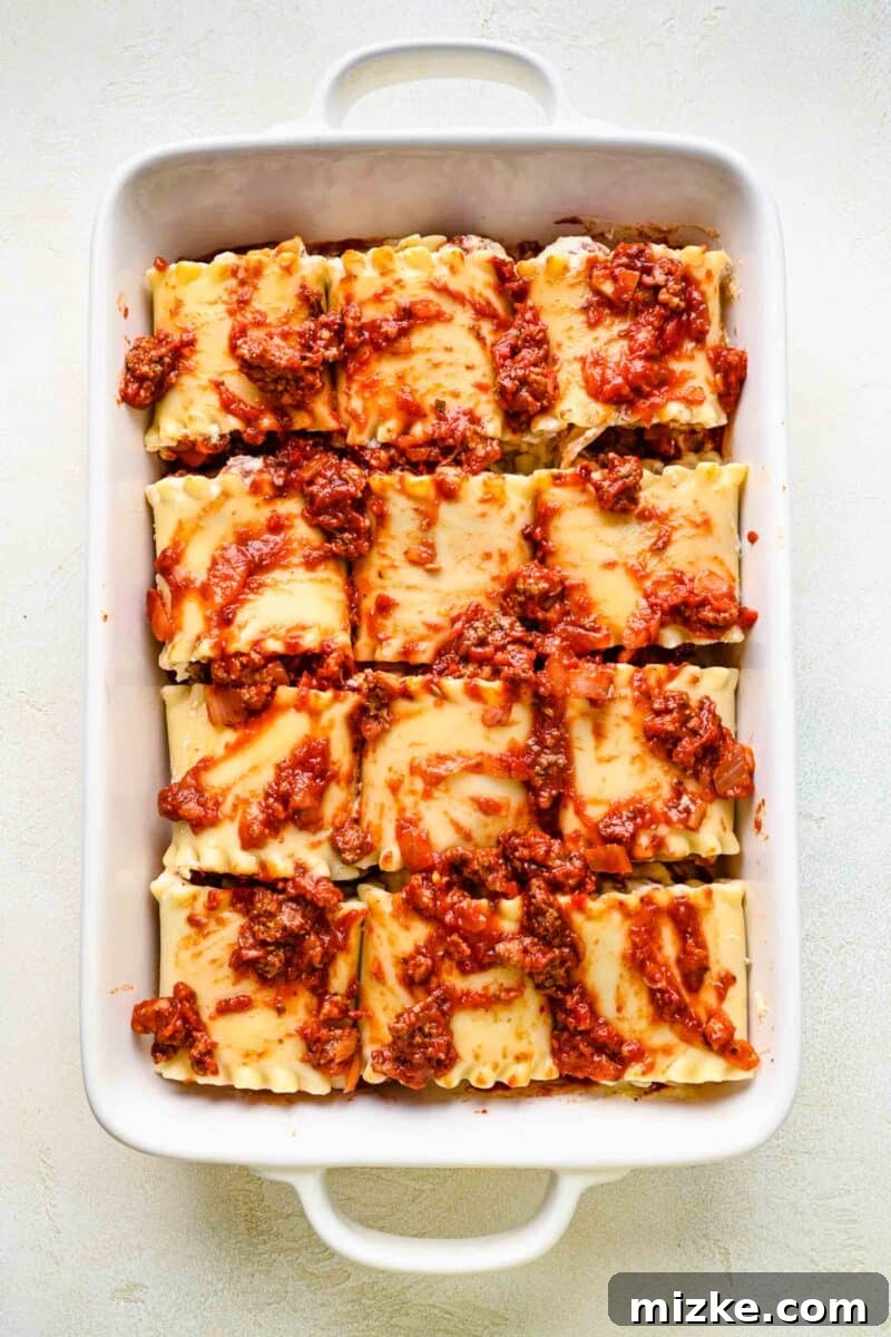 Covering lasagna roll ups with extra meat sauce before baking. Pouring the remaining rich meat sauce over assembled lasagna roll ups in a baking pan.