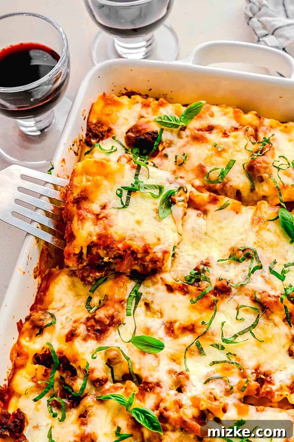 Enjoying homemade lasagna roll ups with a glass of red wine. Overhead shot of a spatula taking a lasagna roll up out of a baking pan, with two glasses of red wine suggesting a complete meal setting.