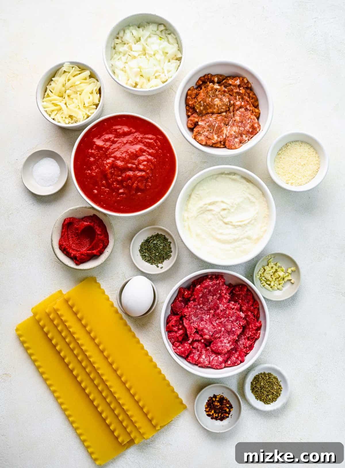 Fresh ingredients laid out for delicious homemade lasagna roll ups. A collection of fresh ingredients for lasagna roll ups, including ground meat, diced onions, garlic, ricotta cheese, and herbs, separated into small bowls.