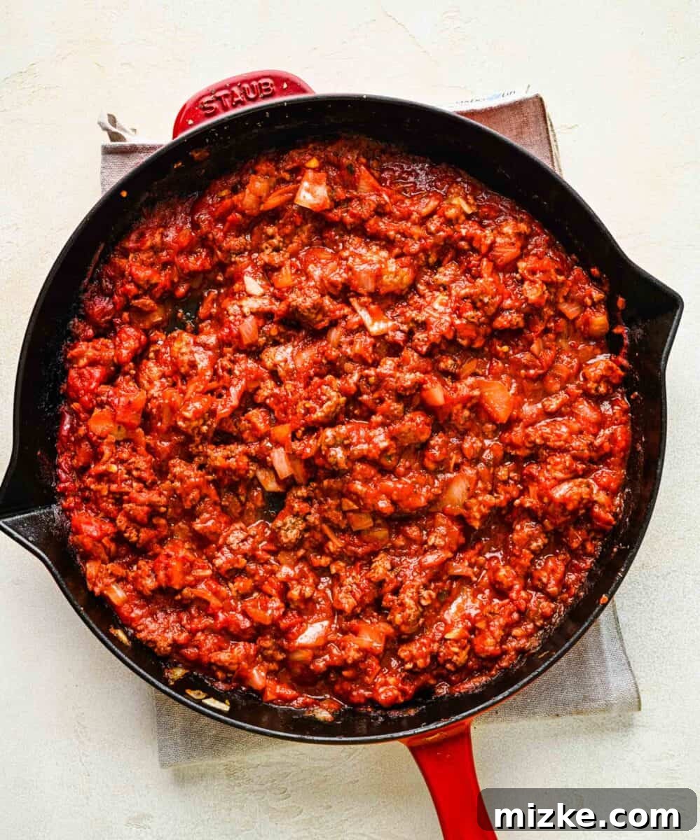 Simmering the rich meat and tomato sauce to perfection. Hearty meat and tomato sauce simmering in a skillet, rich red with visible herbs and meat chunks.