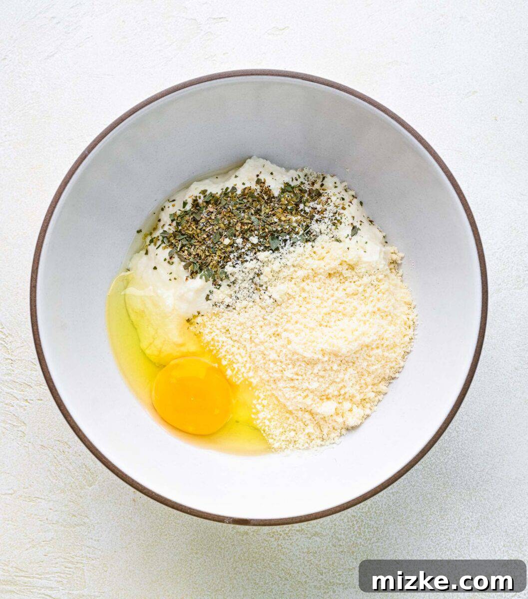 Combining fresh ricotta with egg and Parmesan for a creamy filling. Ingredients for ricotta filling, including cheese, egg, and herbs, being added to a mixing bowl.