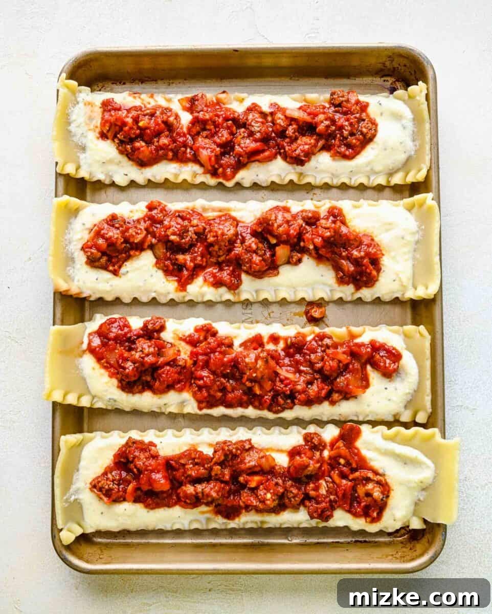 Layering savory meat sauce over ricotta on a lasagna noodle for rolling. A cooked lasagna noodle, already spread with ricotta, now being layered with a rich meat sauce.