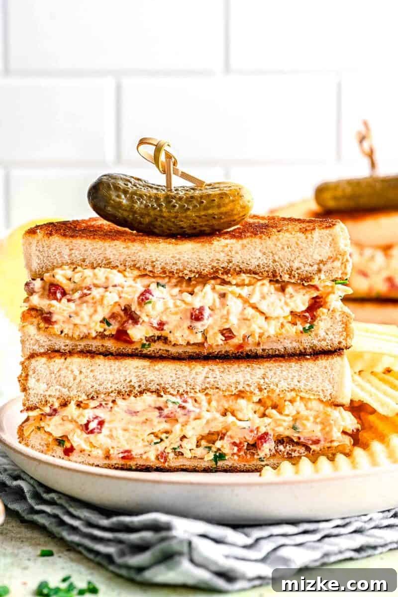 Southern Pimento Perfection 2 pimento cheese sandwich halves stacked on top of each other with a cornichon on top
