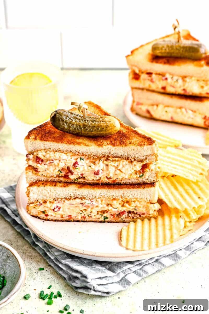Southern Pimento Perfection 5 pimento cheese sandwich halves stacked on top of each other on a plate next to ruffled chips