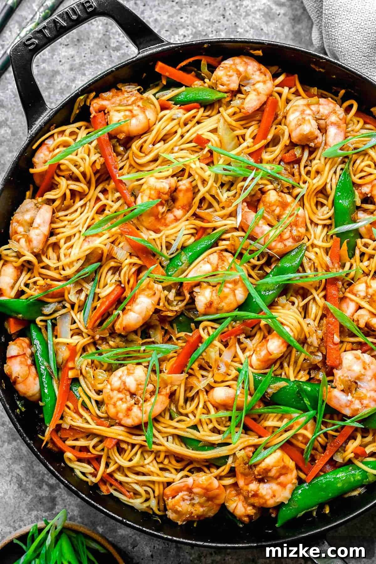 A skillet full of delectable shrimp chow mein, perfectly cooked and ready to enjoy. Overhead shot of freshly cooked shrimp chow mein in a large skillet, ready to be served.