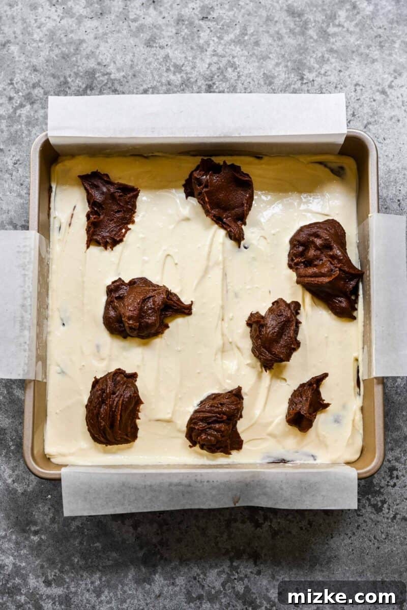 Adding dollops of brownie batter to the top of cream cheese brownies.