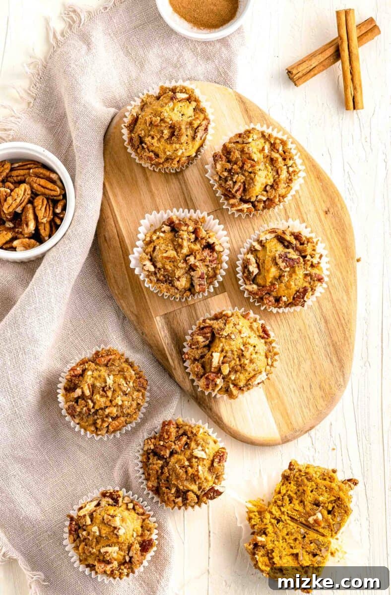 Cozy Pumpkin Pecan Muffins 2 pumpkin pecan muffins on top of a wooden cutting board next to a brown linen towel and cinnamon sticks and spices