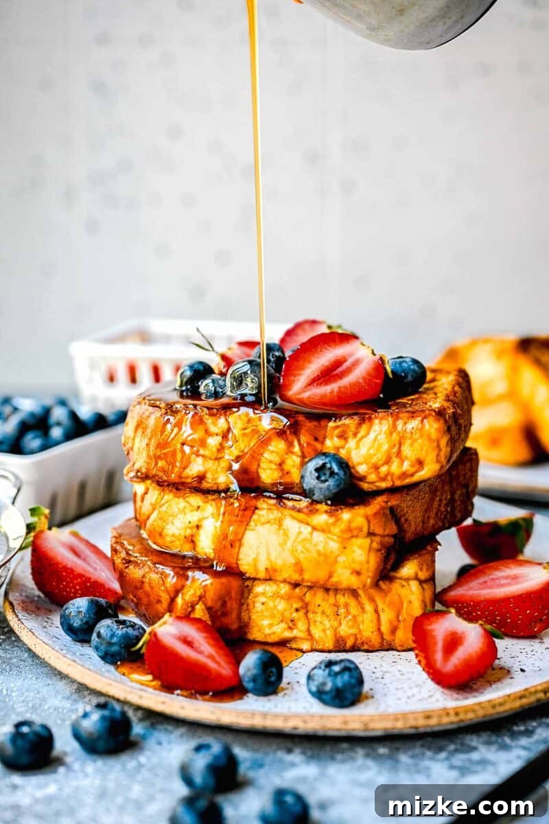 Decadent Pumpkin French Toast 2 syrup being poured onto pumpkin french toast with fresh strawberries and blueberries on top