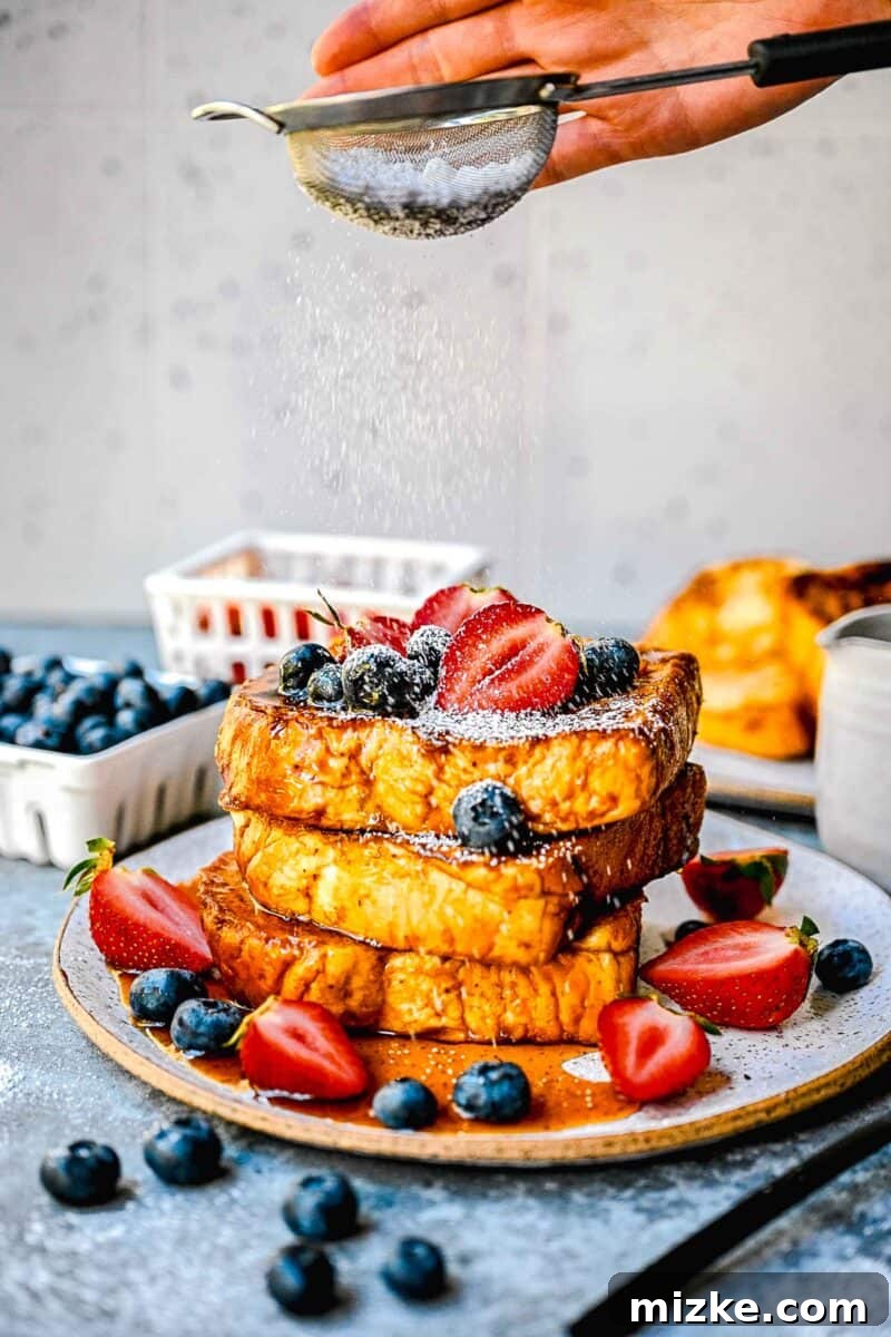Decadent Pumpkin French Toast 5 powdered sugar being sprinkled on top of stack of pumpkin french toast with fresh berries and syrup