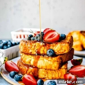 syrup being poured onto pumpkin french toast with fresh strawberries and blueberries on top