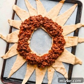 Seasoned and cooked ground beef and cheese mixture arranged in a neat circle on top of the crescent dough base on a metal baking sheet.