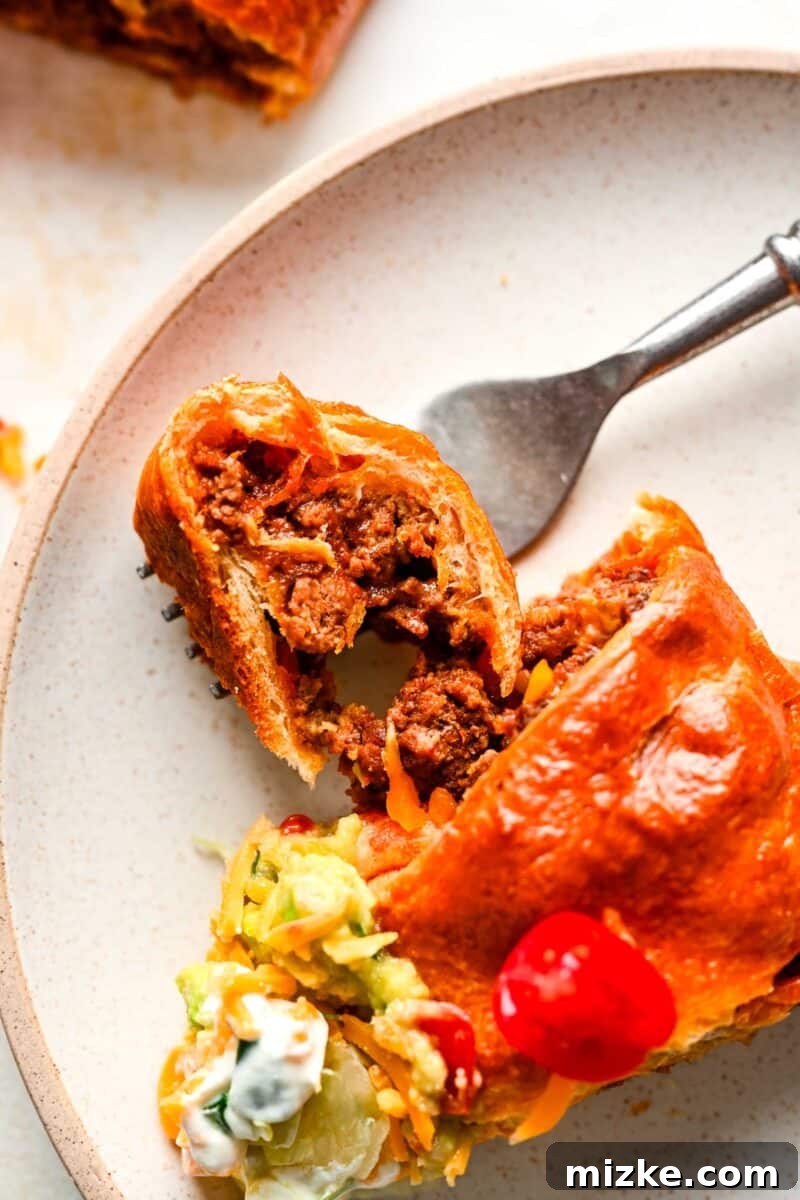 A single slice of taco ring on a ceramic plate, with a fork lifting a piece of the golden-brown crescent dough and ground beef filling.