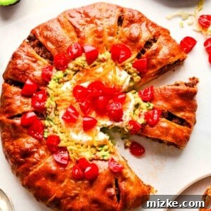 Baked taco ring with guacamole, diced tomatoes, sour cream, and cheddar cheese in the center