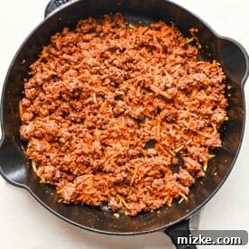Ground beef mixture in a cast iron skillet with shredded cheese added, being stirred to combine.