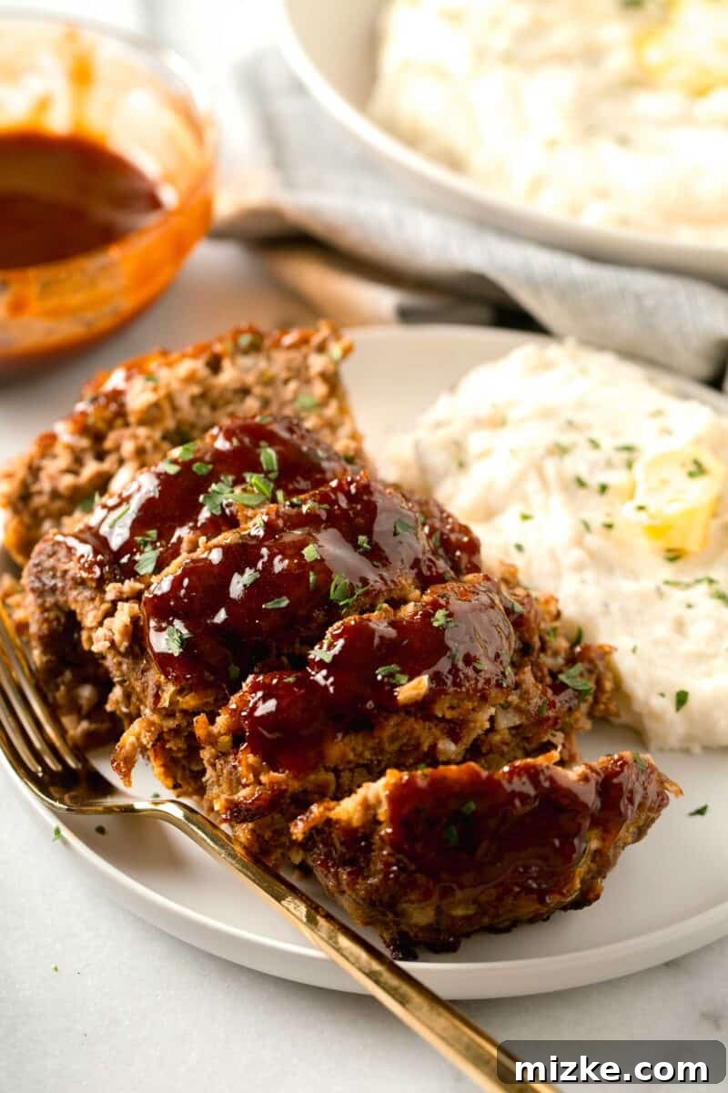 Perfectly sliced air fryer meatloaf on a white plate, accompanied by creamy mashed potatoes and a gold fork.