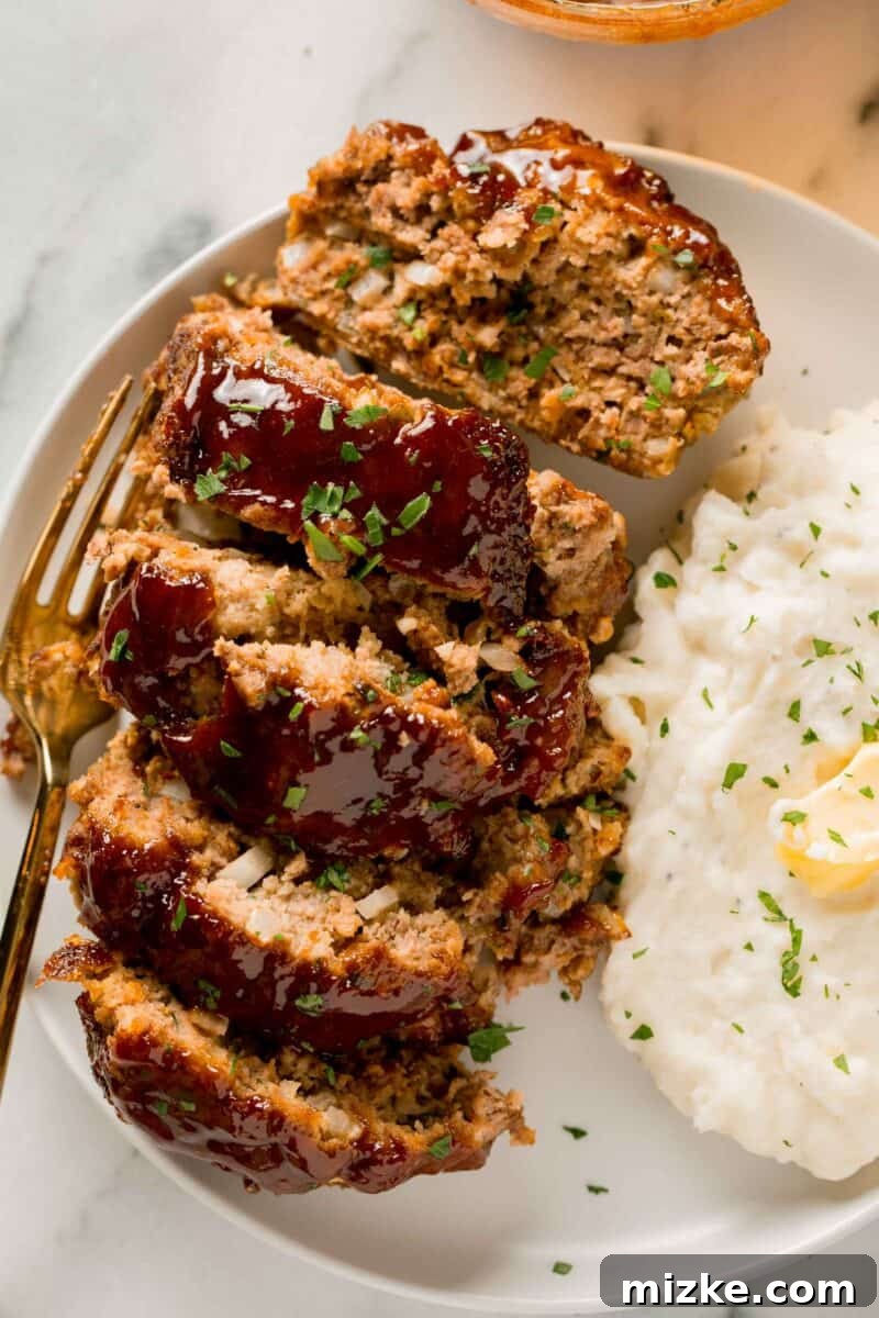 Appetizing slices of air fryer meatloaf presented on a white plate, perfectly complemented by a side of fluffy mashed potatoes.