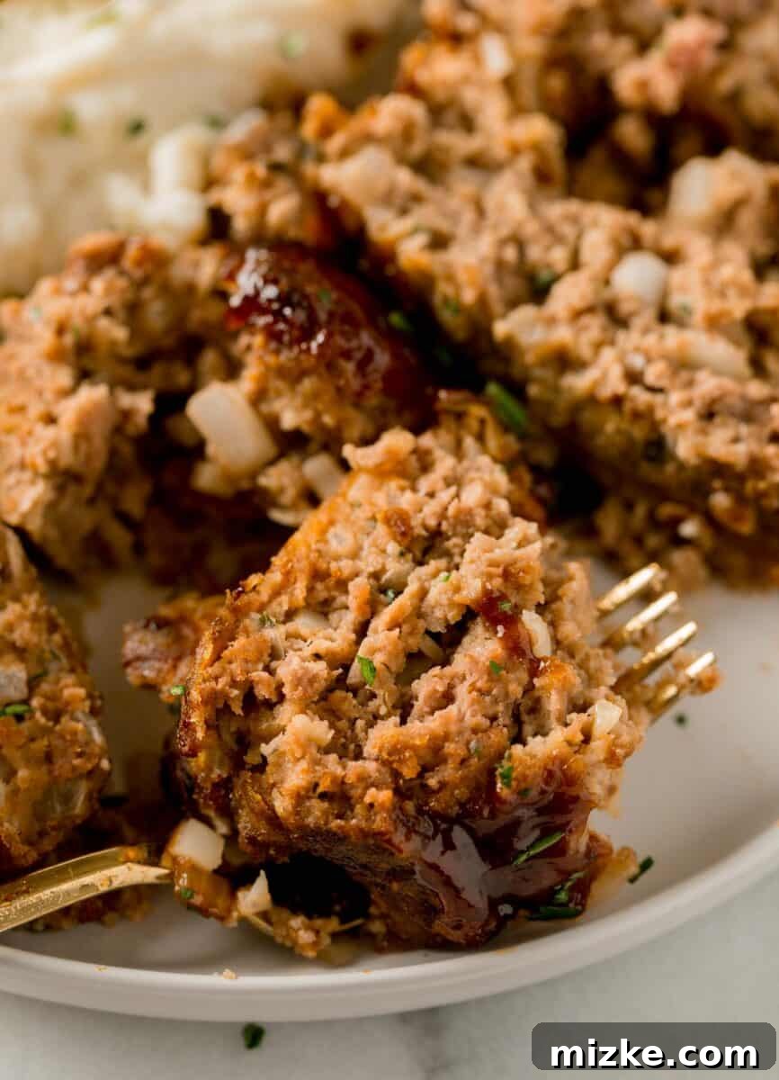 A delectable piece of glazed meatloaf expertly perched on the tines of a metal fork, ready to be enjoyed.