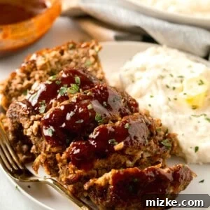 meatloaf slices on a large white rimmed plate with mashed potatoes on the side and a gold metal fork
