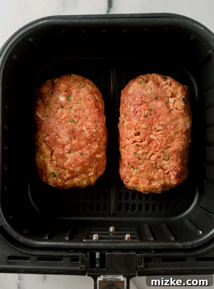 Two perfectly shaped raw meatloaves placed side-by-side in the basket of an air fryer, ready for cooking.