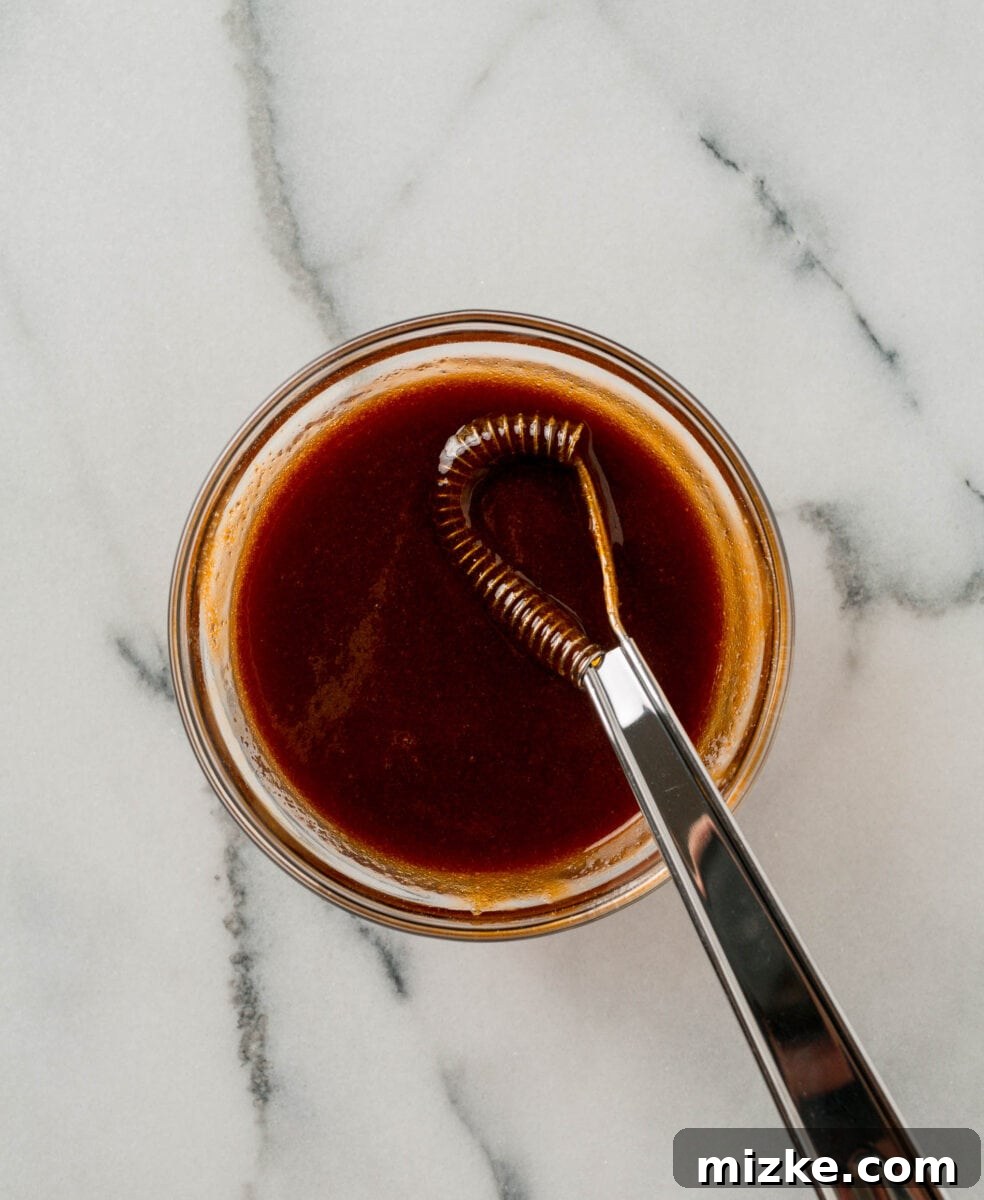 The savory and sweet meatloaf glaze, perfectly whisked together in a clear glass bowl with a metal whisk.